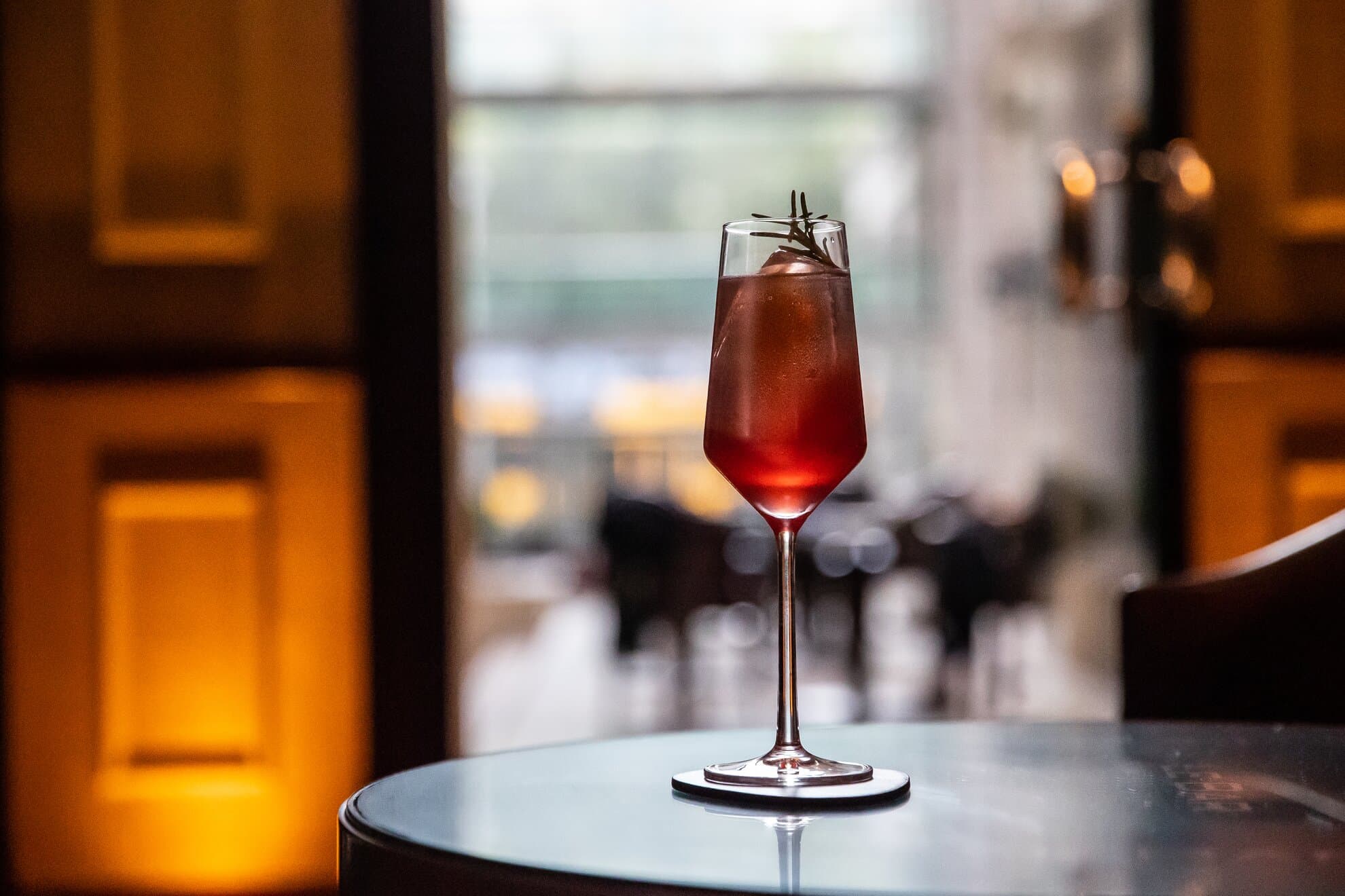 Cocktail på et bord i Le Bar i Corinthia Budapest med varm belysning i bakgrunnen.